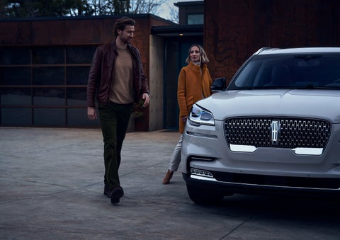 A man and a woman approaching a 2024 Lincoln Aviator® SUV, which illuminates certain lights when they are close | Wallace Lincoln in Fort Pierce FL