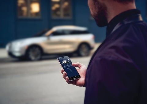 A person is shown interacting with a smartphone to connect to a Lincoln vehicle across the street. | Wallace Lincoln in Fort Pierce FL