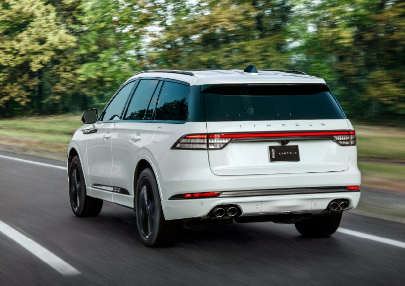 A white 2026 Lincoln Aviator® SUV is being driven away down a road lined with colorful trees. | Wallace Lincoln in Fort Pierce FL