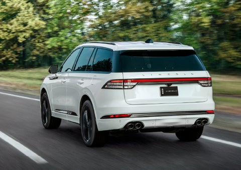 A white 2026 Lincoln Aviator® SUV is being driven away down a road lined with colorful trees. | Wallace Lincoln in Fort Pierce FL