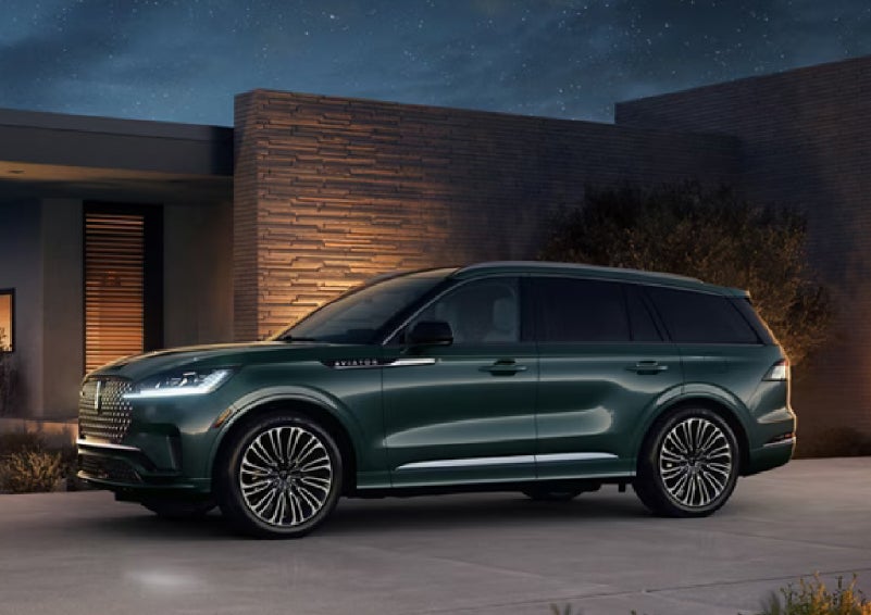 A green 2027 Lincoln Aviator® SUV is parked outside a contemporary home. | Wallace Lincoln in Fort Pierce FL