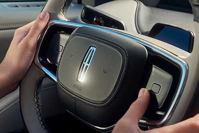 A man holding the steering wheel inside a Lincoln vehicle.